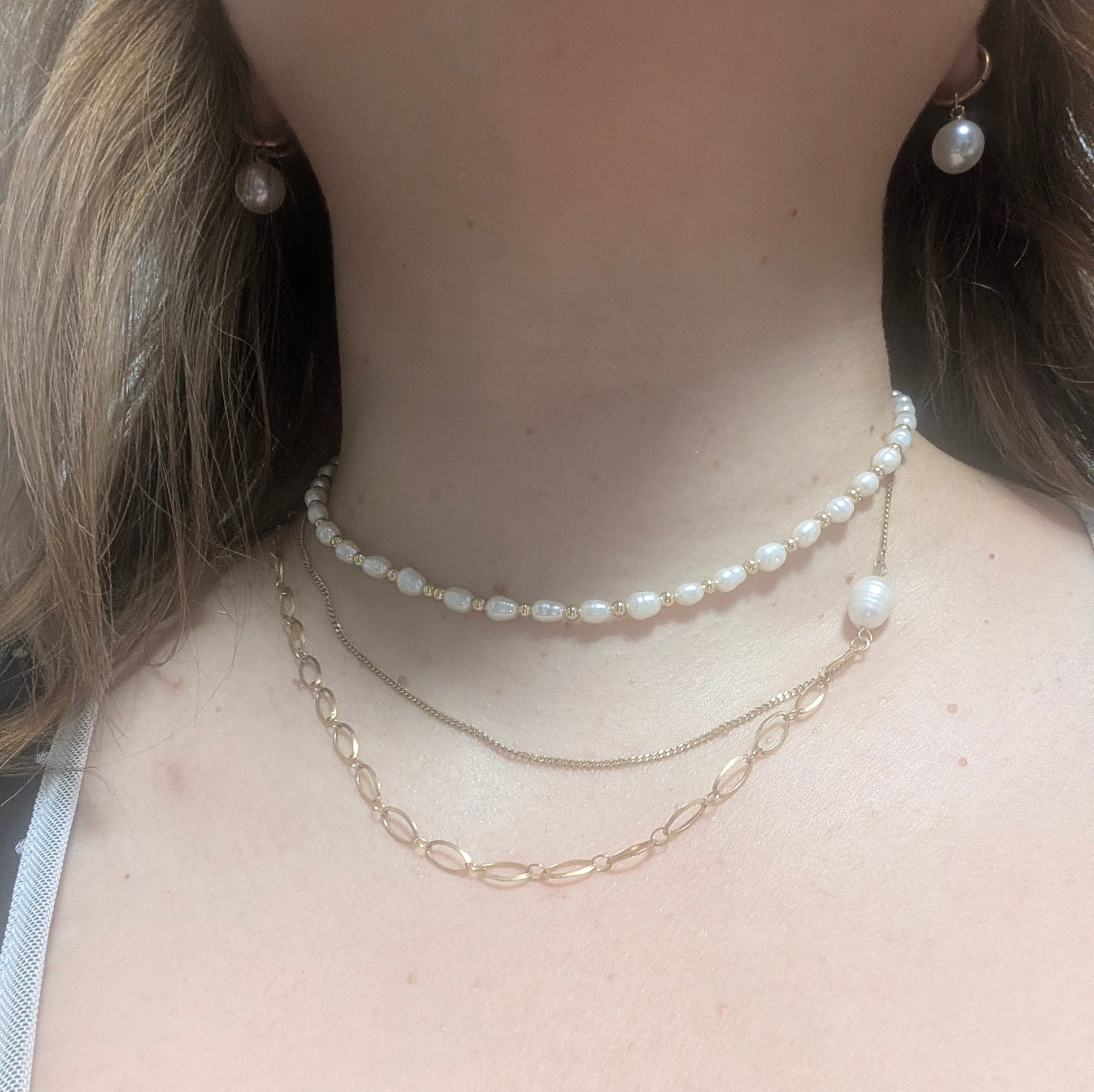 Pearl necklace and earrings on a person's neck and ears