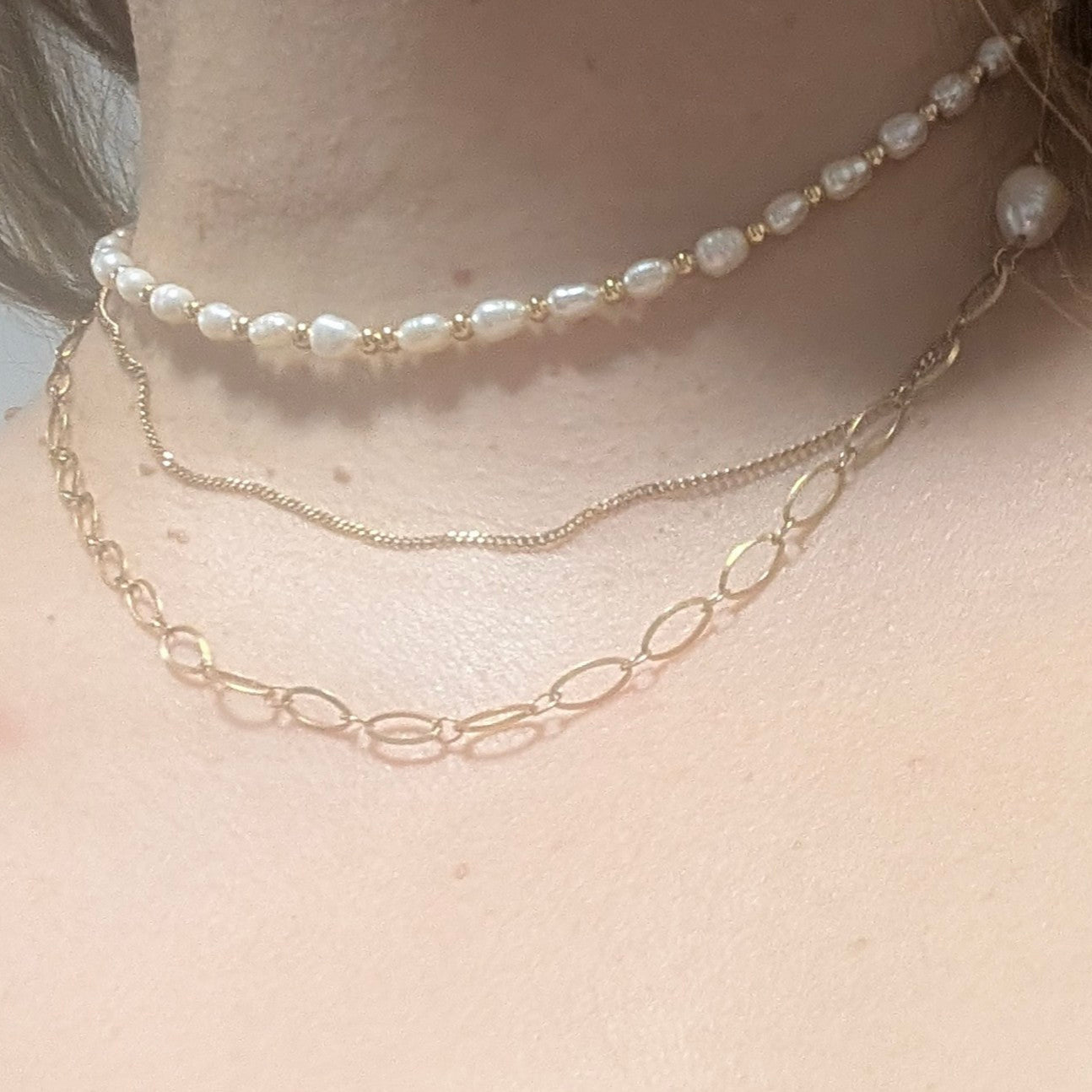 Two necklaces on a person's neck with a pearl necklace on top and a gold chain necklace on the bottom.